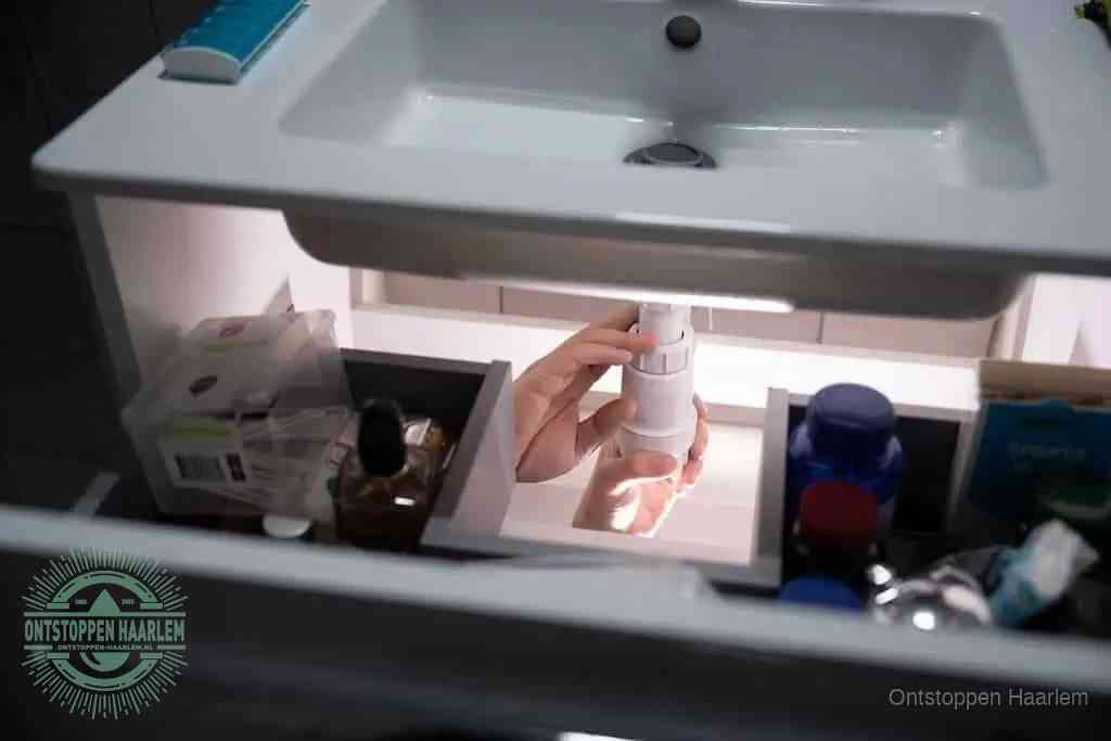 Een pompfles met zeep boven een wastafel, de heet water en afwasmiddel-methode om een vetprop in de afvoer los te maken in Haarlem