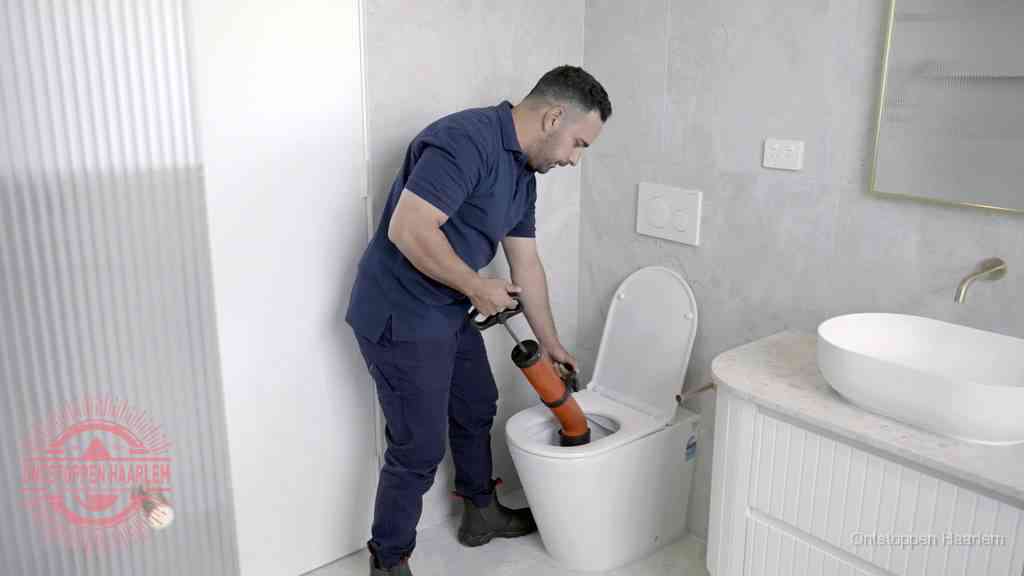 Een monteur buigt over een wandcloset en duwt met de hand een persluchtontstopper in de toiletpot om de verstopping handmatig los te maken in Haarlem