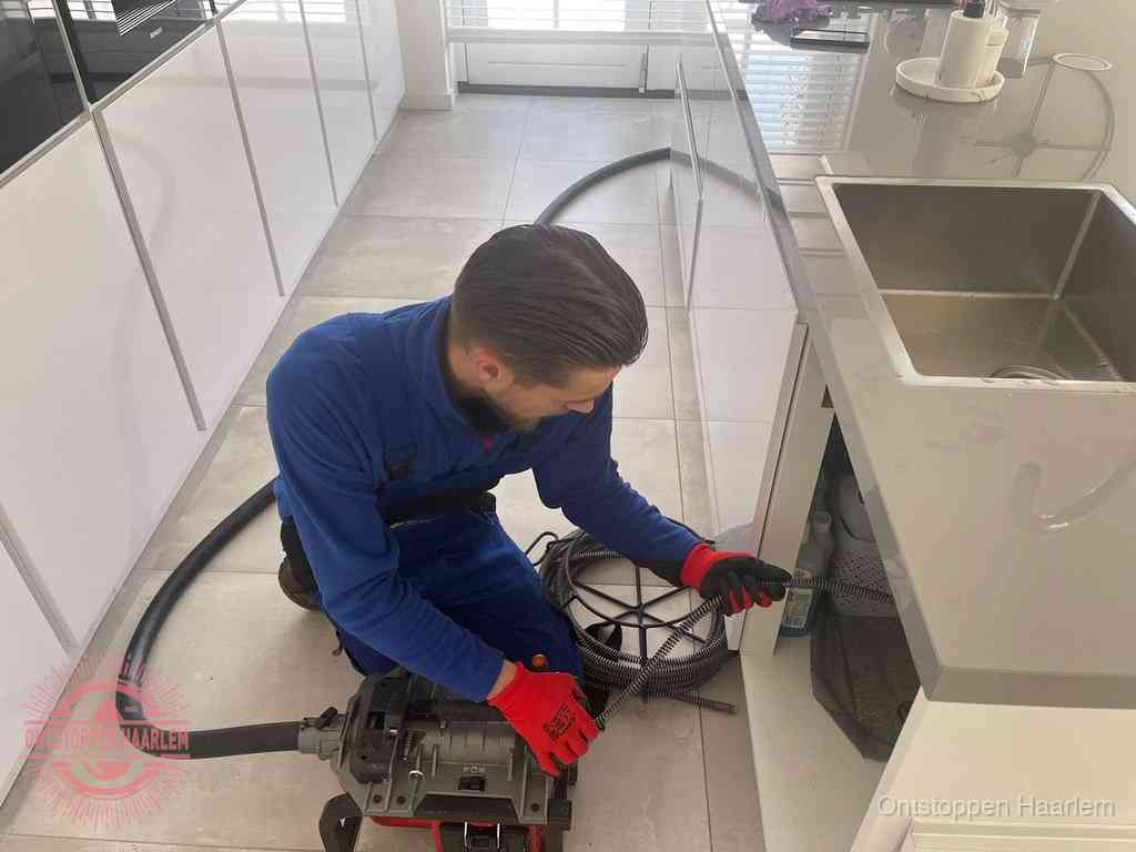 Een monteur ontstopt de keukenafvoer onder de spoelbak met een elektrische veermachine in Haarlem