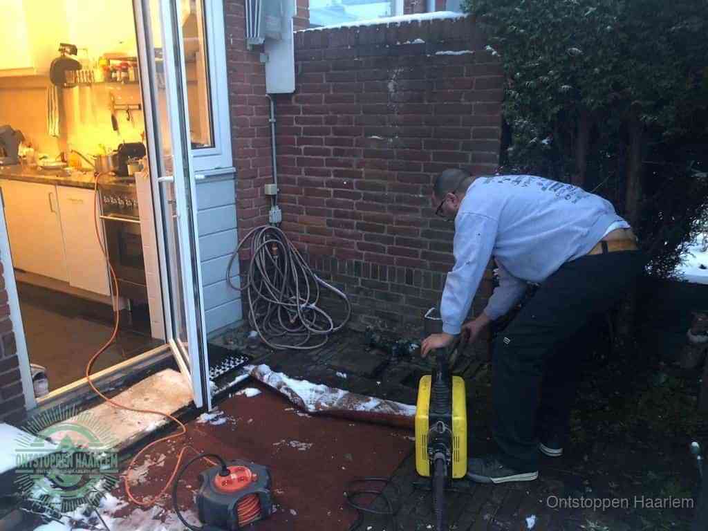Een monteur werkt buiten bij een open riool-/grondput met een elektrische ontstoppingsmachine om een verborgen afvoerprobleem op te sporen in Haarlem