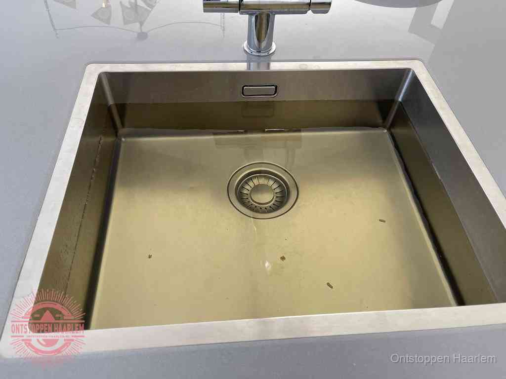 Stilstaand water in een rvs spoelbak dat niet wegloopt, een duidelijk signaal van een gootsteenverstopping in Haarlem