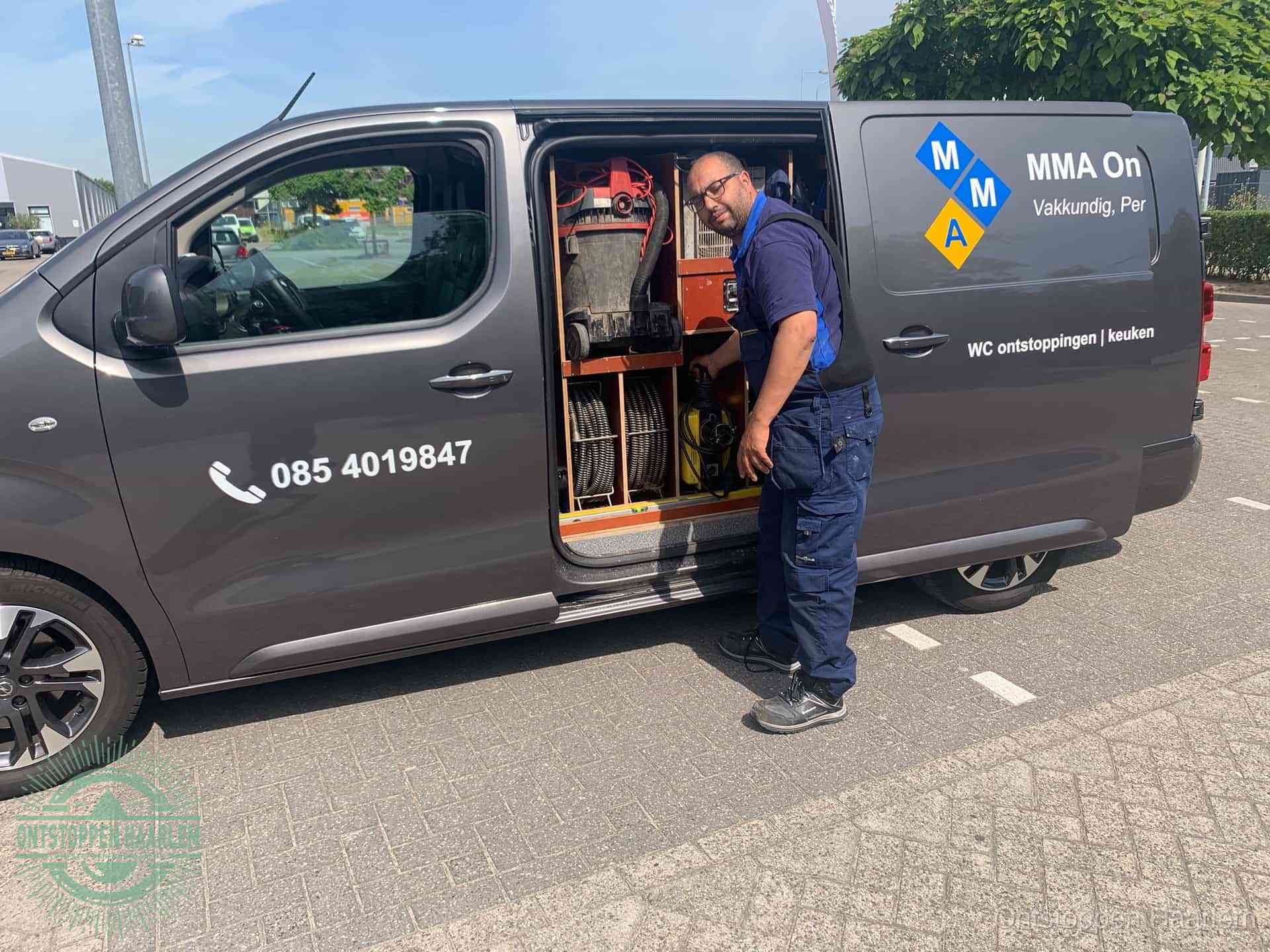 Een monteur bij de open schuifdeur van zijn bedrijfsbus op een parkeerplaats, klaar om de oorzaak van terugkerende afvoerverstoppingen aan te pakken in Haarlem