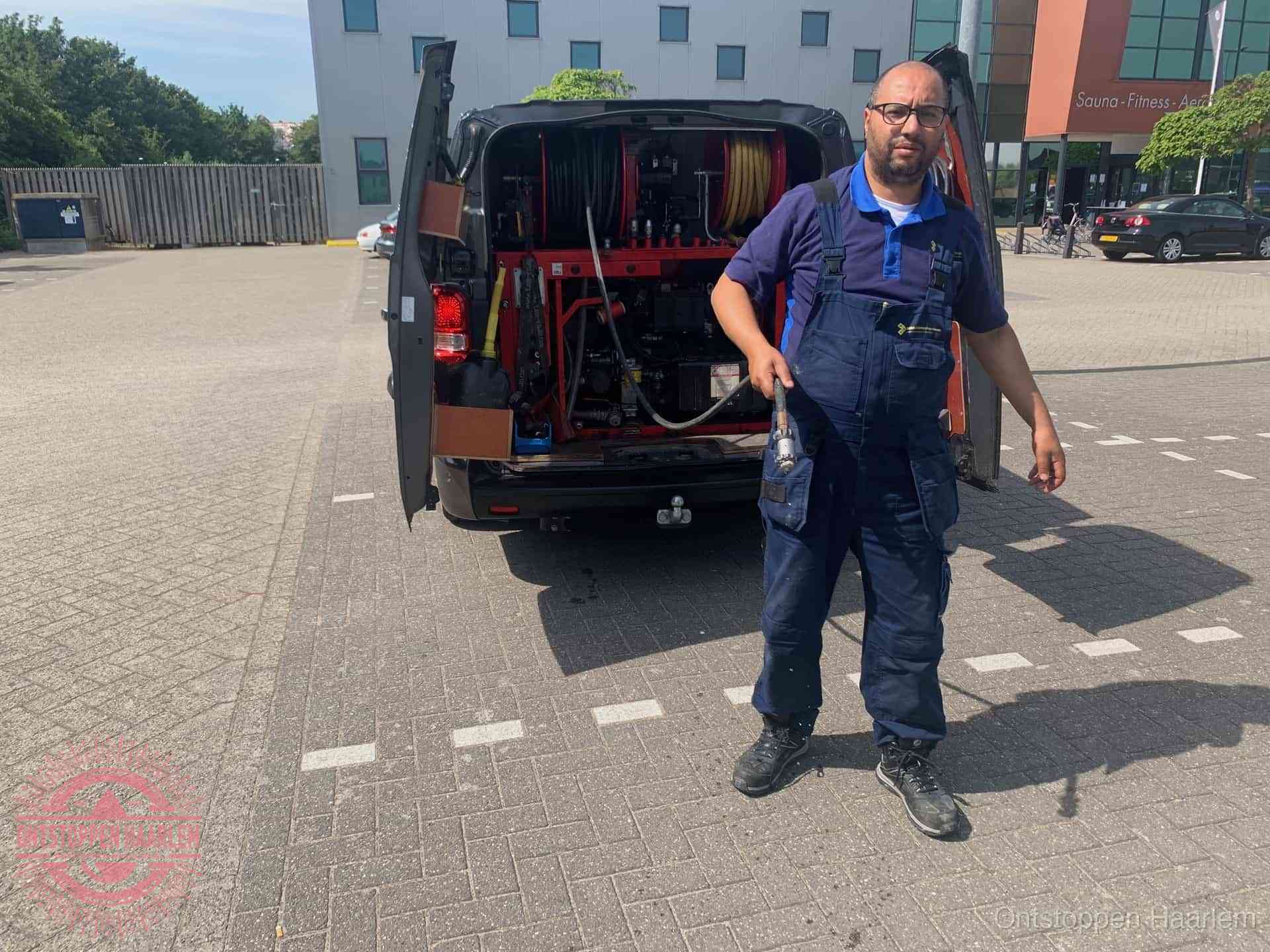 Een monteur bij zijn bestelbus met een hogedruk- en rioolreinigingsunit, klaar om de oorzaak van terugkerende wc-verstoppingen aan te pakken in Haarlem