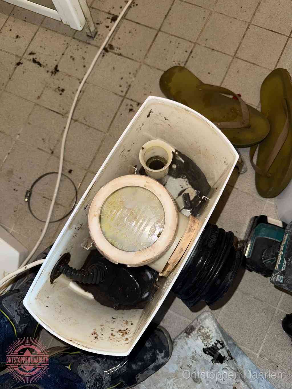 Een gedemonteerde toiletpot op de vloer met ontstoppingsveer en gereedschap ernaast, het verwijderen van een vastzittend voorwerp uit de wc in Haarlem