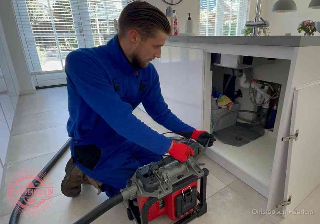 Een monteur voert een professionele elektrische ontstoppingsmachine in de afvoer onder de spoelbak tijdens het gootsteen ontstoppen in Haarlem