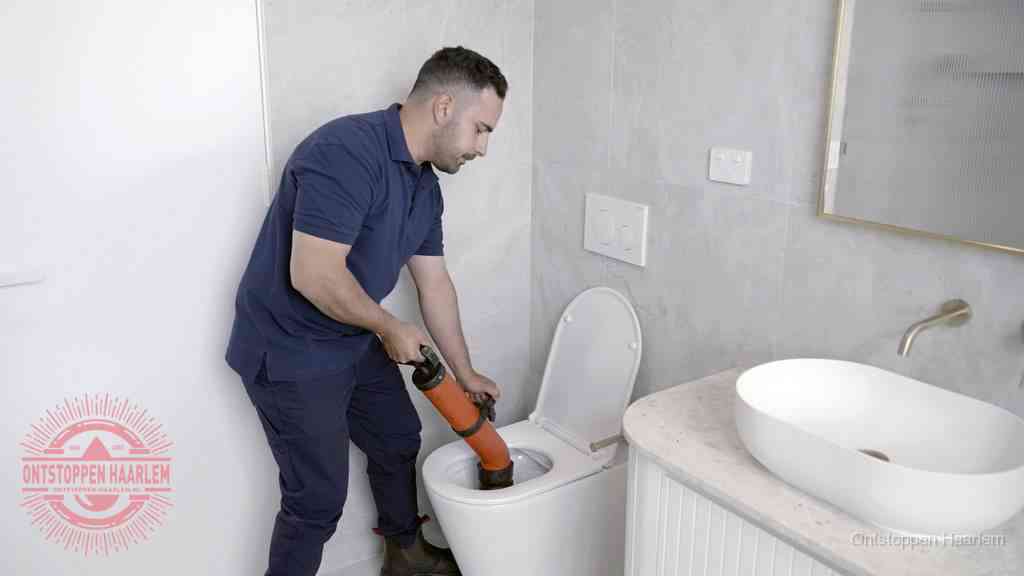 Een man gebruikt een handmatige luchtdruk-ontstopper in een modern betegeld toilet om zelf de wc te ontstoppen in Haarlem